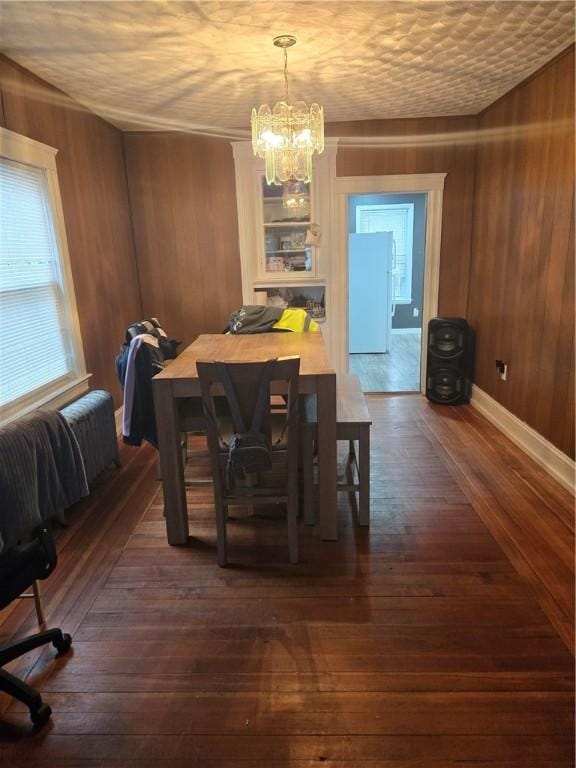 dining area with a notable chandelier, wood walls, and dark hardwood / wood-style flooring