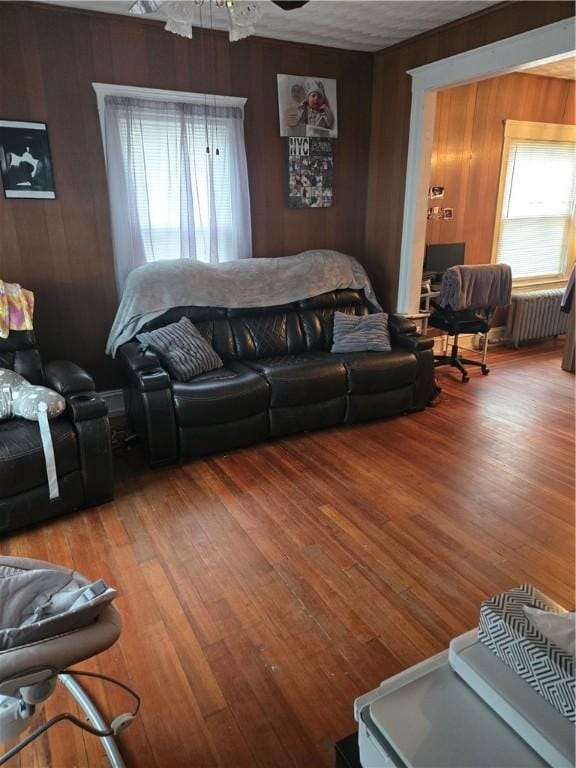 living room with ceiling fan, radiator heating unit, wooden walls, and hardwood / wood-style flooring