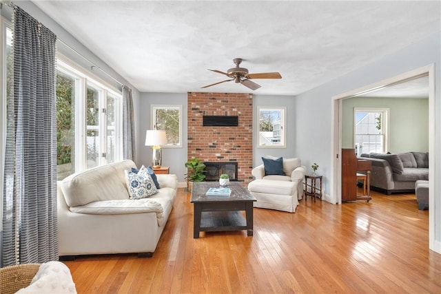 living room featuring a fireplace, ceiling fan, and light wood-type flooring