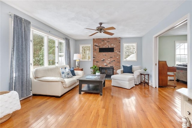 living room featuring ceiling fan, a brick fireplace, and light hardwood / wood-style flooring