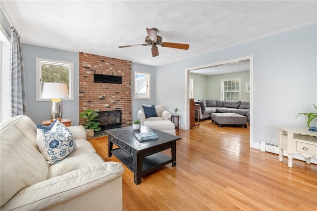 living room with a brick fireplace, a baseboard heating unit, ceiling fan, and light hardwood / wood-style flooring