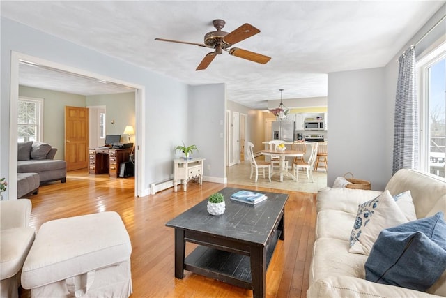 living room featuring a baseboard heating unit, ceiling fan, and light wood-type flooring