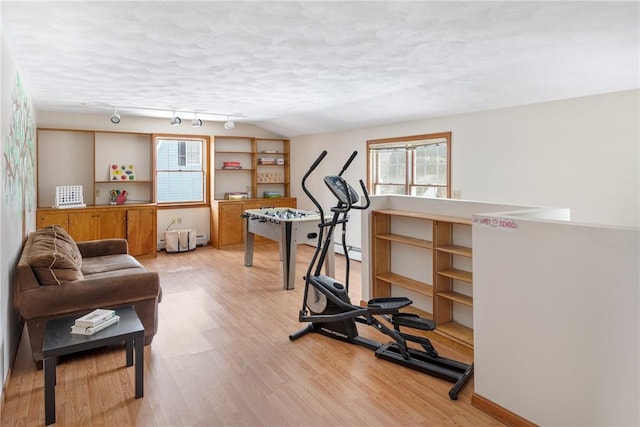 workout area with rail lighting, vaulted ceiling, a textured ceiling, and light hardwood / wood-style floors