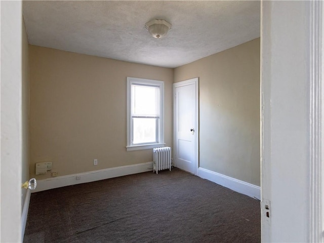 spare room with dark carpet and radiator