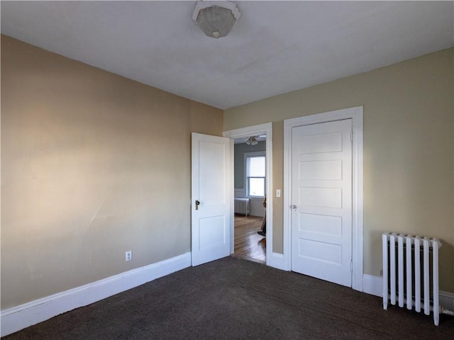 unfurnished bedroom featuring radiator and dark carpet