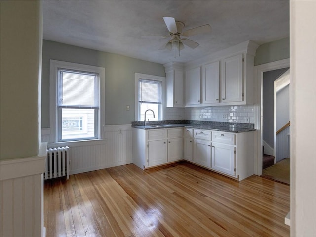 kitchen with backsplash, white cabinetry, radiator, and light hardwood / wood-style flooring