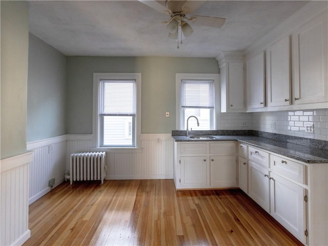 kitchen featuring radiator heating unit, white cabinetry, sink, backsplash, and light hardwood / wood-style flooring