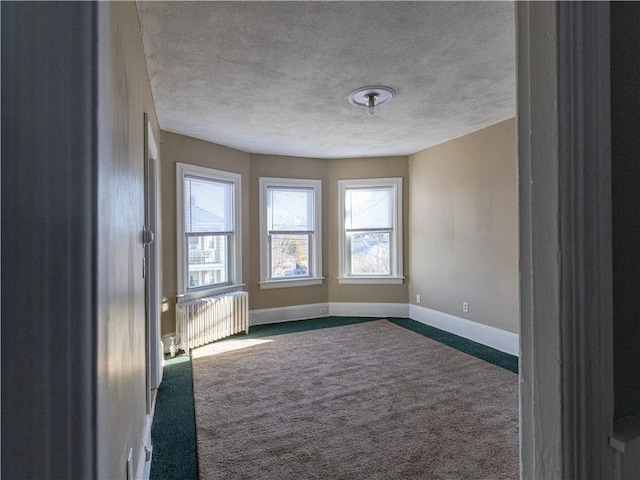 spare room featuring a textured ceiling, radiator heating unit, and dark colored carpet