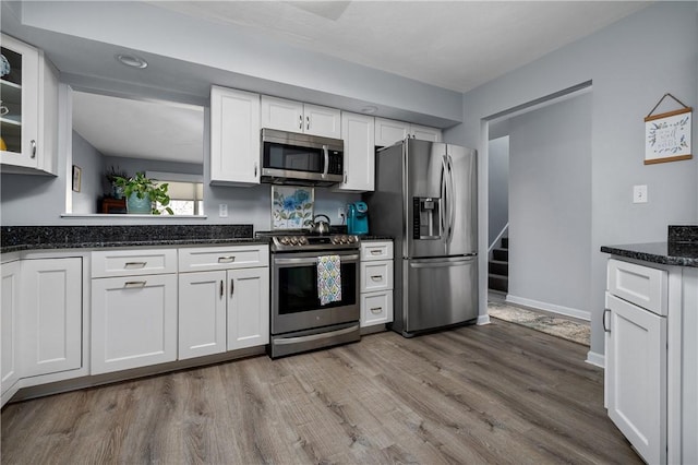 kitchen featuring dark stone countertops, stainless steel appliances, white cabinetry, and light hardwood / wood-style floors