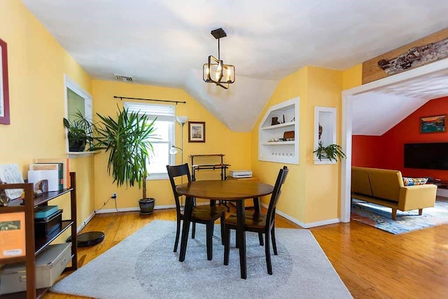 dining room featuring light wood-type flooring, built in shelves, a notable chandelier, and vaulted ceiling