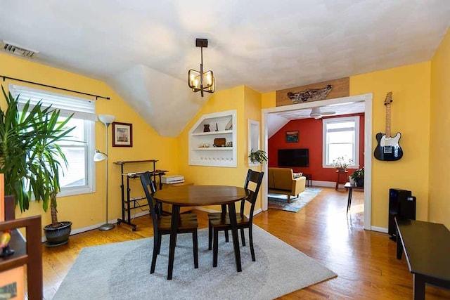 dining space featuring built in shelves, a wealth of natural light, light hardwood / wood-style floors, and vaulted ceiling