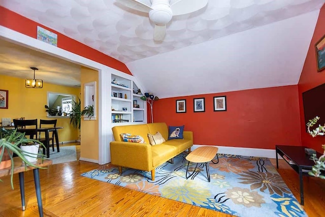 living room featuring built in shelves, ceiling fan, vaulted ceiling, and wood-type flooring