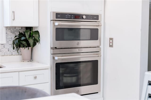 kitchen featuring white cabinetry, stainless steel double oven, and tasteful backsplash