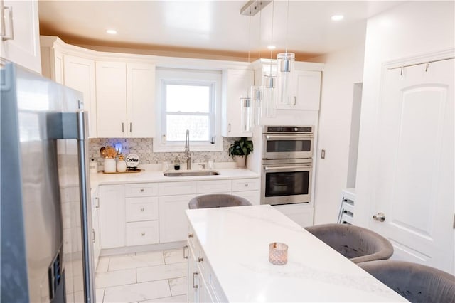 kitchen with white cabinetry, hanging light fixtures, decorative backsplash, sink, and stainless steel appliances