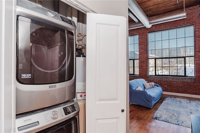 laundry area featuring stacked washer / drying machine, brick wall, gas water heater, and dark wood-type flooring