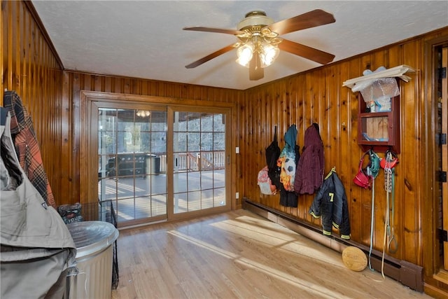 doorway to outside featuring light hardwood / wood-style floors, wood walls, baseboard heating, and a textured ceiling