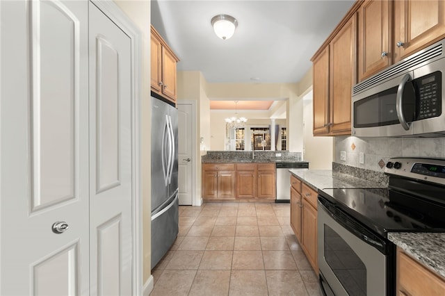 kitchen featuring a notable chandelier, appliances with stainless steel finishes, light tile patterned floors, dark stone countertops, and backsplash