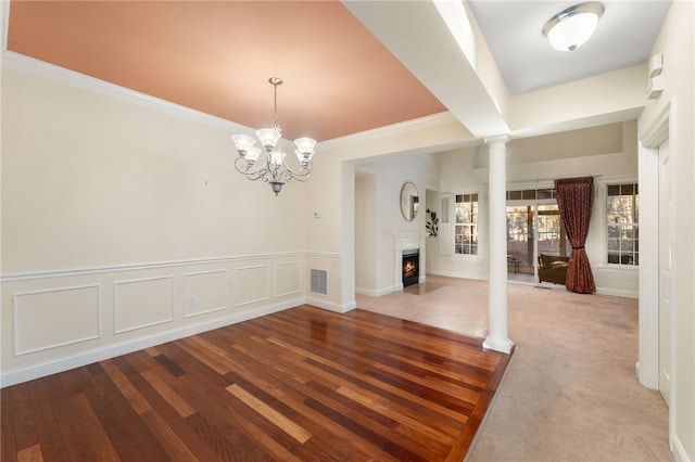 unfurnished dining area featuring wood-type flooring, ornate columns, and an inviting chandelier