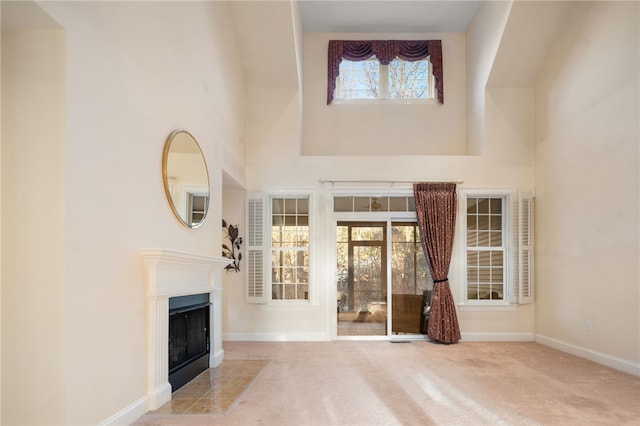 unfurnished living room with a towering ceiling, a tile fireplace, and light carpet