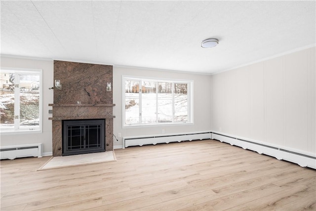 unfurnished living room with a baseboard heating unit, plenty of natural light, light wood-style flooring, and crown molding