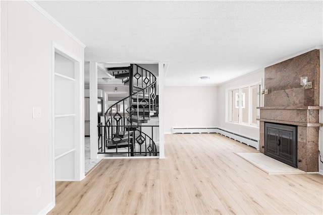 unfurnished living room with crown molding, light wood-style floors, a baseboard heating unit, a large fireplace, and stairs