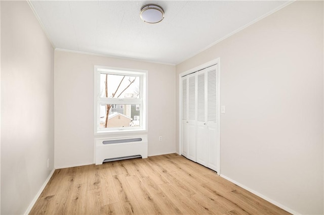 unfurnished bedroom featuring baseboards, light wood-style floors, ornamental molding, a closet, and radiator heating unit