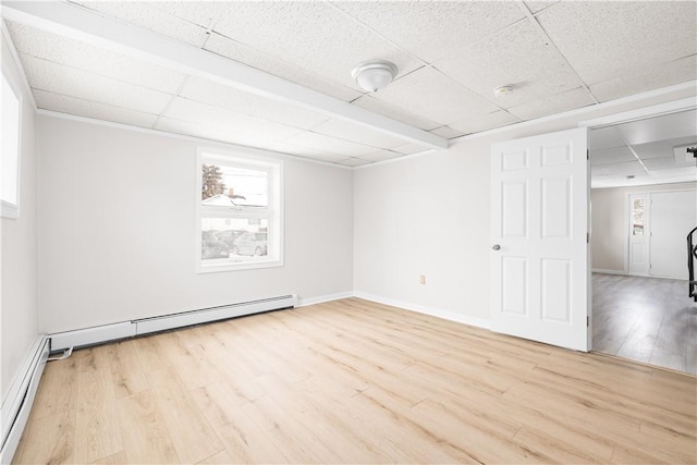 unfurnished room with a baseboard heating unit, a drop ceiling, baseboards, and light wood-style floors