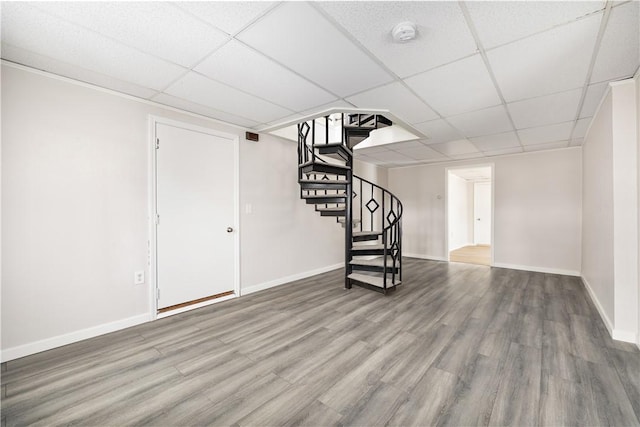 finished basement featuring baseboards, stairway, a drop ceiling, and wood finished floors