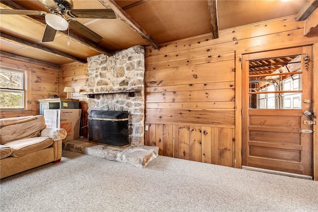 carpeted living room featuring beamed ceiling, a fireplace, wood ceiling, wooden walls, and ceiling fan