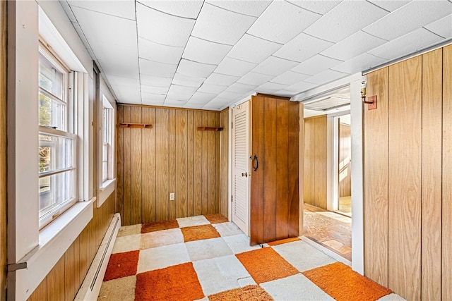 unfurnished bedroom featuring baseboard heating, multiple windows, and wood walls