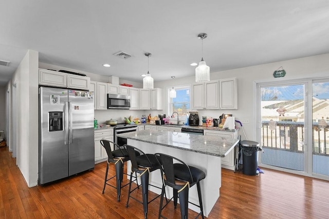 kitchen featuring decorative light fixtures, white cabinets, a breakfast bar, a kitchen island, and stainless steel appliances