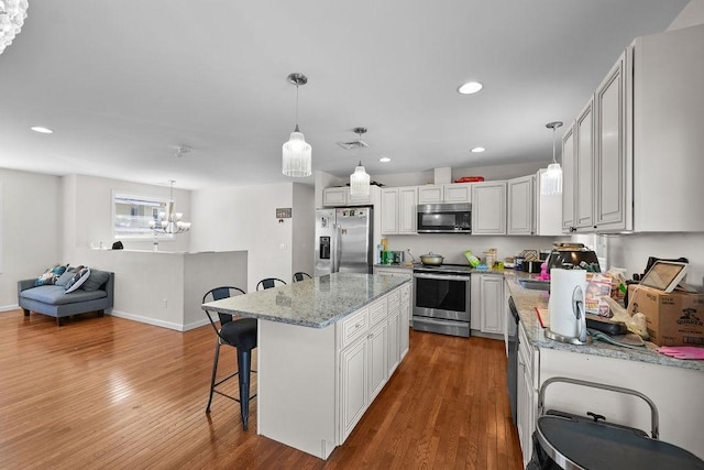 kitchen with decorative light fixtures, white cabinetry, hardwood / wood-style floors, a kitchen island, and stainless steel appliances