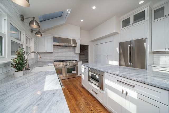 kitchen with sink, high end appliances, white cabinets, decorative backsplash, and wall chimney exhaust hood