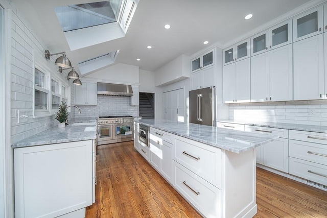 kitchen with white cabinetry, high end appliances, a center island, and wall chimney range hood