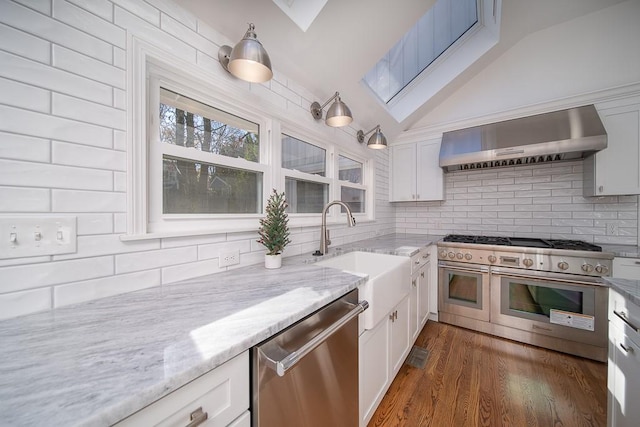 kitchen with appliances with stainless steel finishes, white cabinetry, wall chimney range hood, and a sink