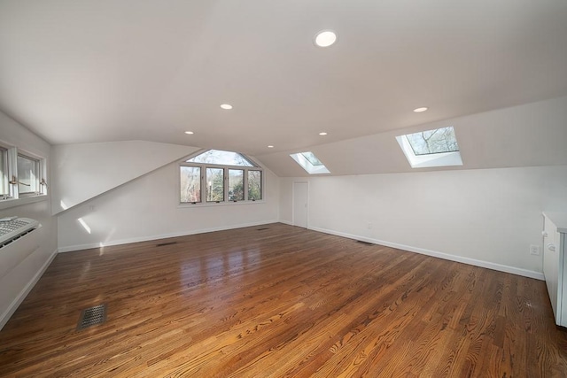 additional living space featuring vaulted ceiling with skylight, wood finished floors, visible vents, and baseboards