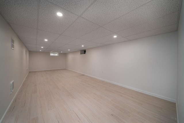 basement featuring a drop ceiling and light hardwood / wood-style flooring