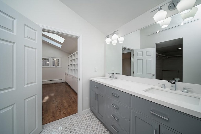 bathroom featuring double vanity, vaulted ceiling with skylight, a baseboard radiator, and a sink