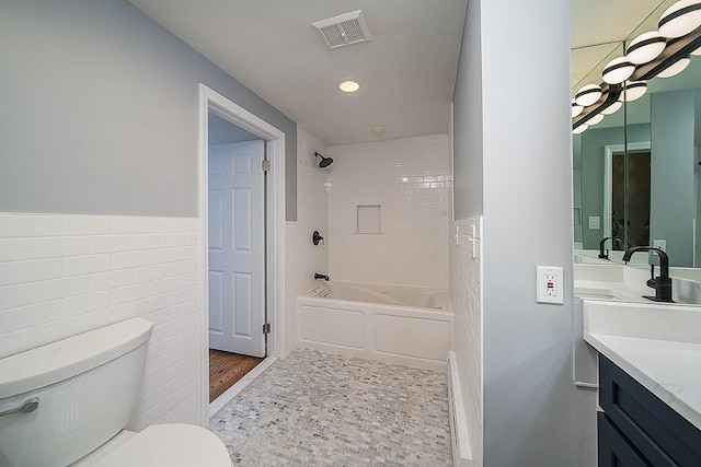 full bathroom with visible vents, toilet, vanity, bathing tub / shower combination, and tile walls