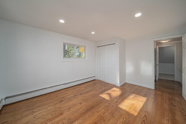 unfurnished bedroom with a baseboard heating unit, wood finished floors, recessed lighting, a closet, and baseboards