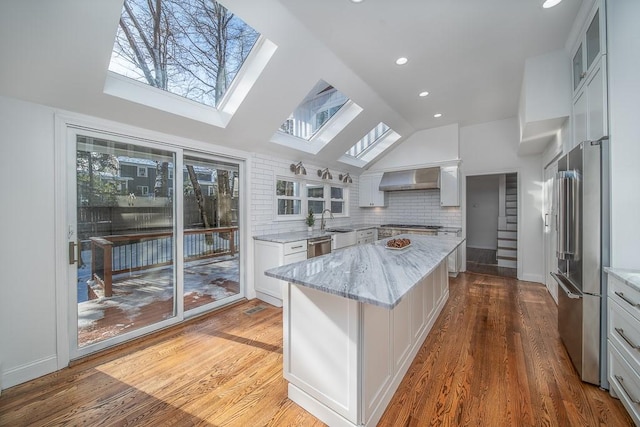 kitchen featuring lofted ceiling with skylight, a kitchen island, stainless steel appliances, wall chimney range hood, and a healthy amount of sunlight