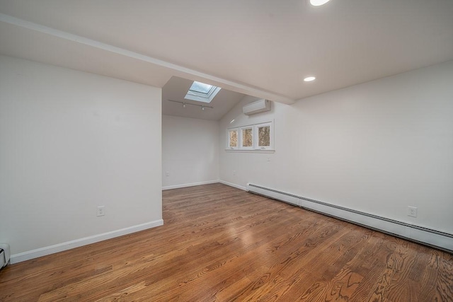 unfurnished room featuring a wall unit AC, wood finished floors, baseboards, a baseboard radiator, and lofted ceiling with skylight