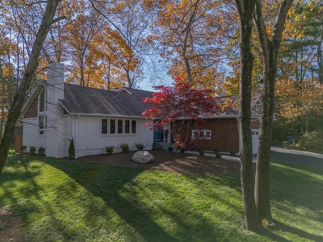 rear view of property with a chimney, a lawn, a garage, and a shingled roof