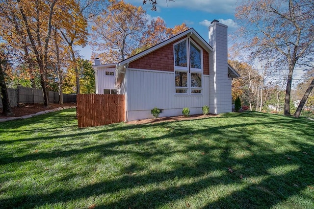 view of side of home with a chimney, a yard, and fence