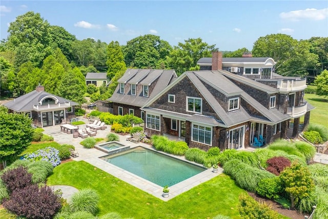 rear view of property with a swimming pool with hot tub, a patio area, and a lawn