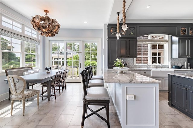 kitchen with light stone counters, hanging light fixtures, decorative backsplash, and a kitchen island