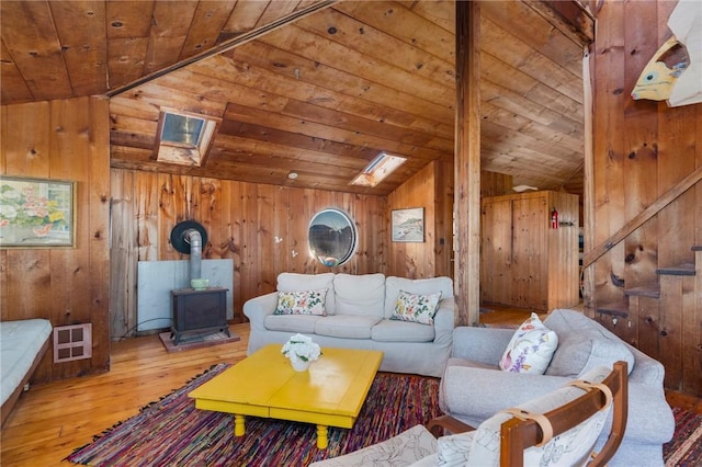 living room with hardwood / wood-style floors, wooden walls, lofted ceiling with skylight, wooden ceiling, and a wood stove