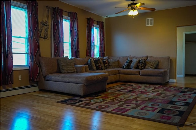 living room featuring ceiling fan, wood-type flooring, a baseboard radiator, and a healthy amount of sunlight