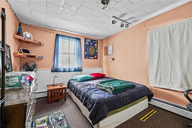 bedroom with wooden walls, dark carpet, and a baseboard heating unit