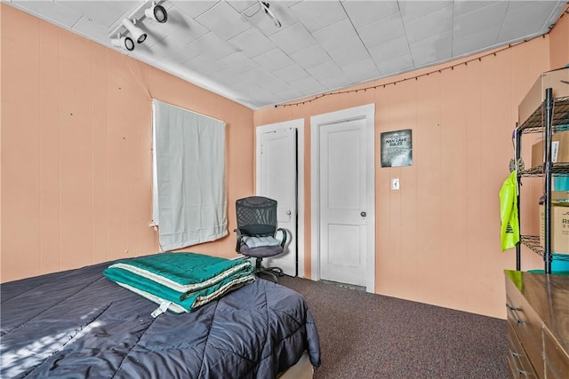 bedroom with carpet floors, wooden walls, and track lighting